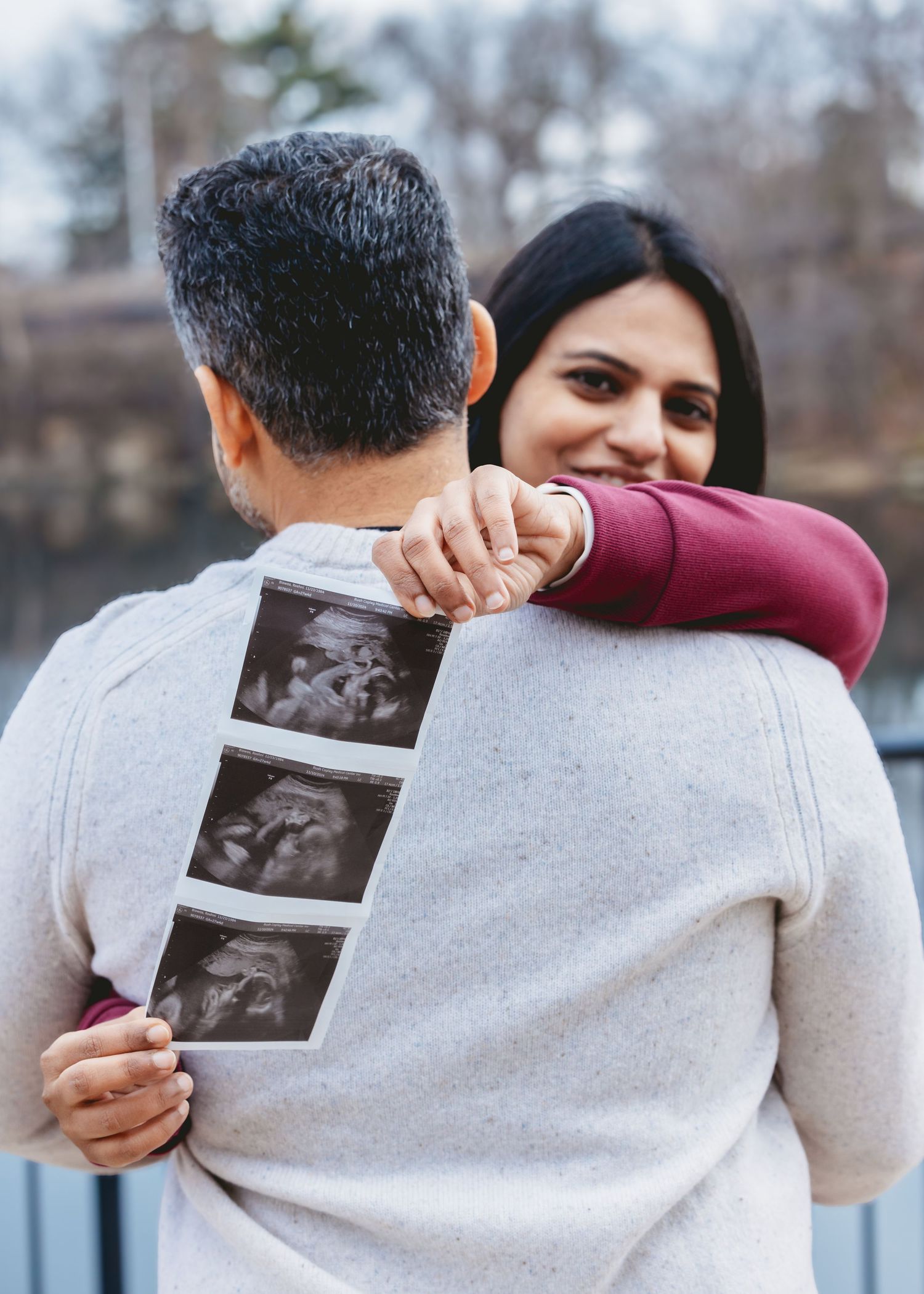 Pregnant announcement photo of couple embracing, man holding ultrasound strip while woman smiles joyfully.