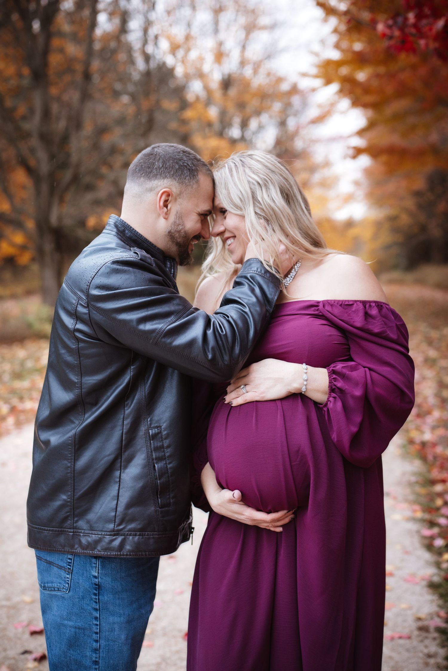 Loving couple touching foreheads tenderly during fall maternity photography session outdoors.
