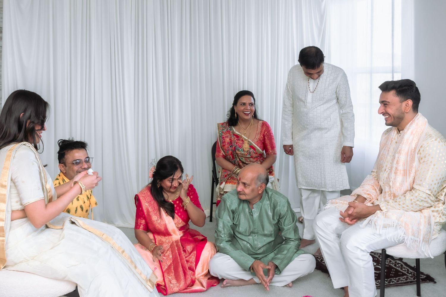 A joyful group of family members in traditional Indian attire gather and laugh during a wedding celebration.