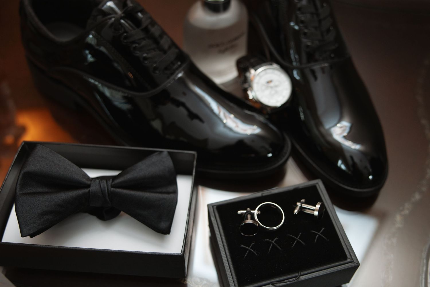 Groom's wedding accessories including black bow tie, cufflinks, watch, and patent shoes.