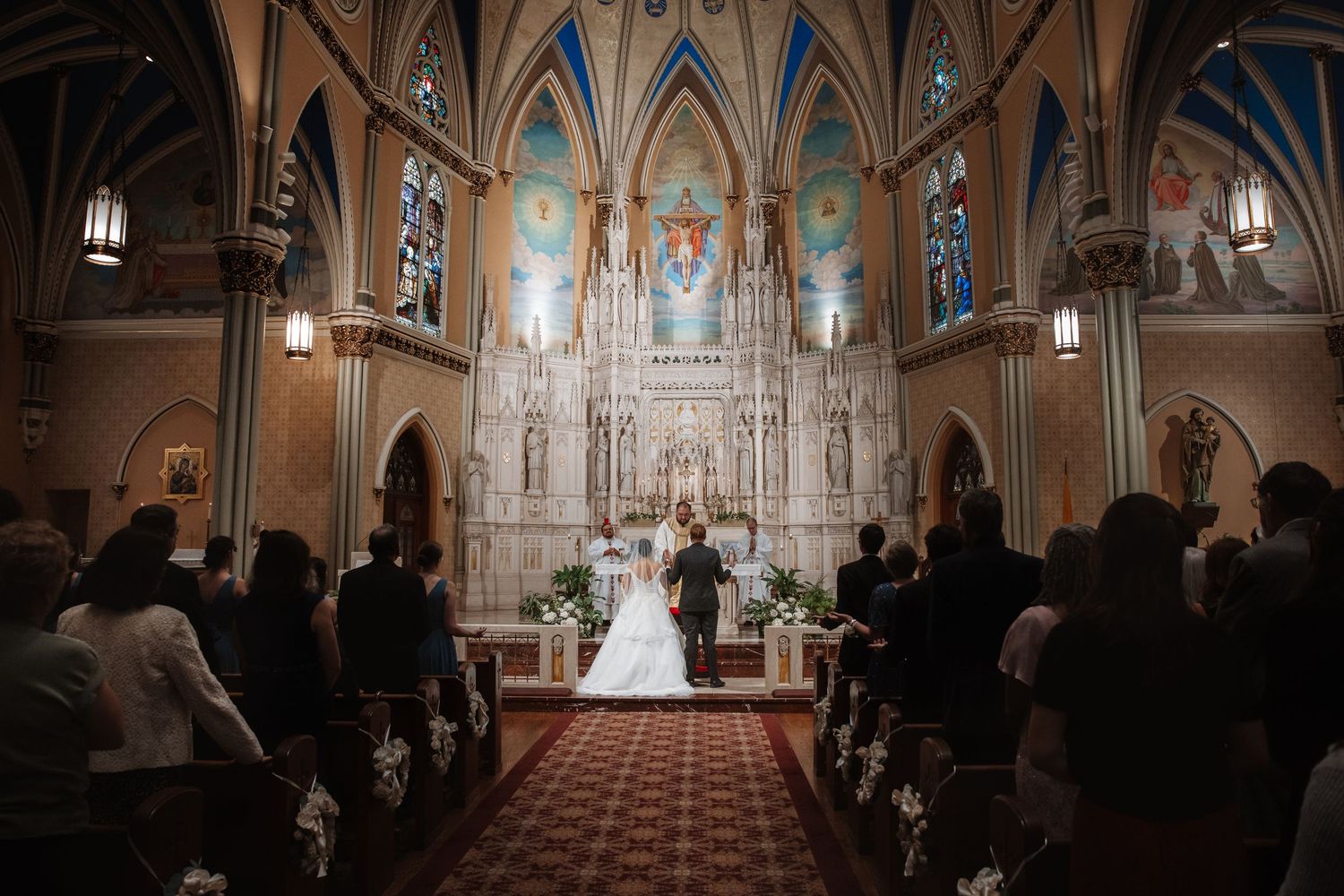 Wedding ceremony at ornate church with guests seated in pews.
