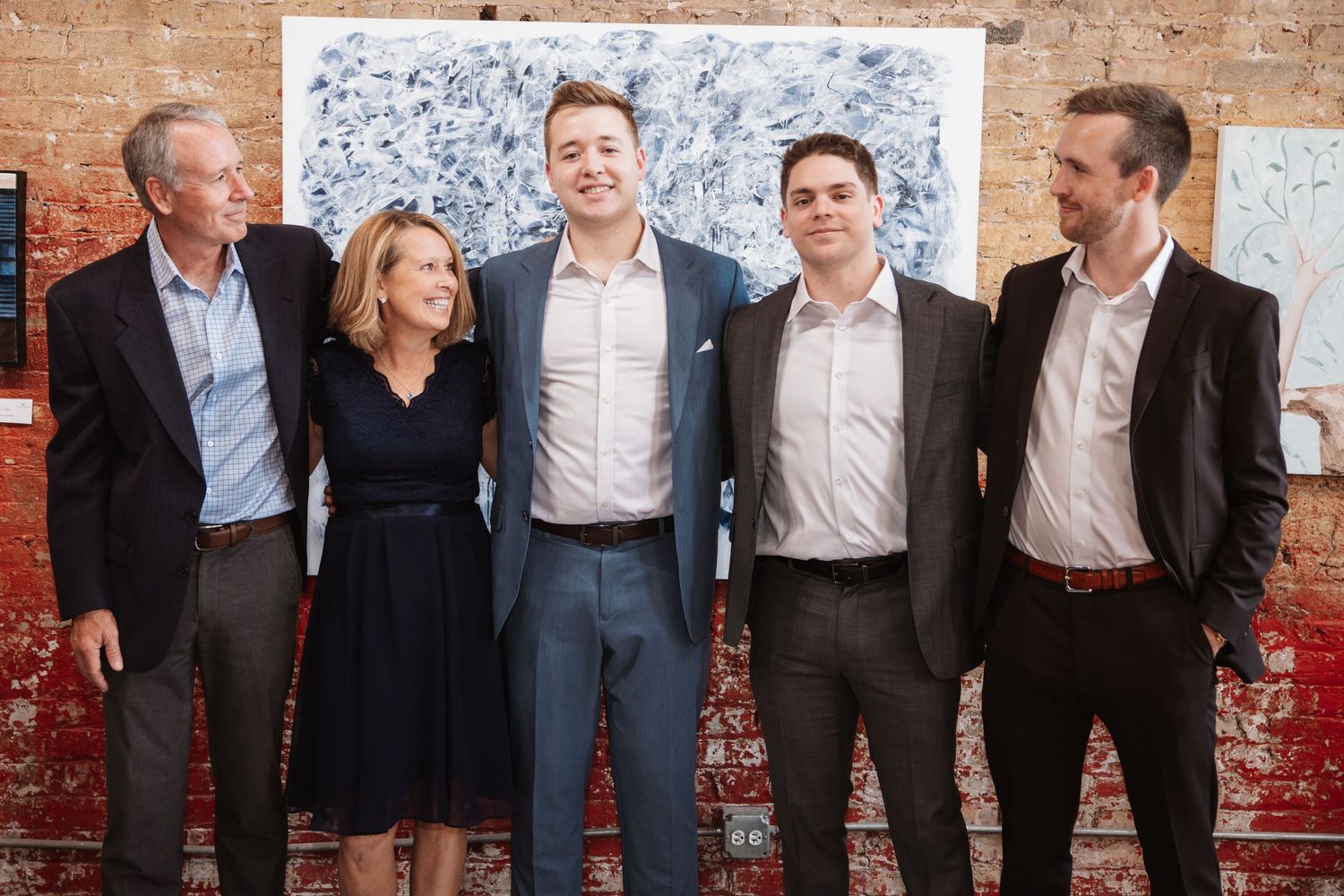 Five well-dressed guests smile together at an art gallery event in front of abstract artwork.