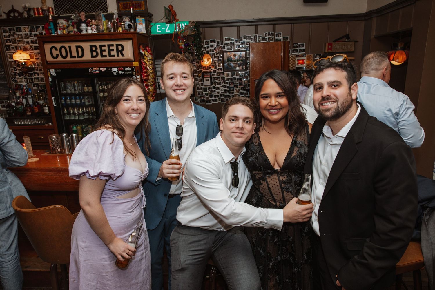 A group of five friends smile and pose together at a bar during a lively celebration event.