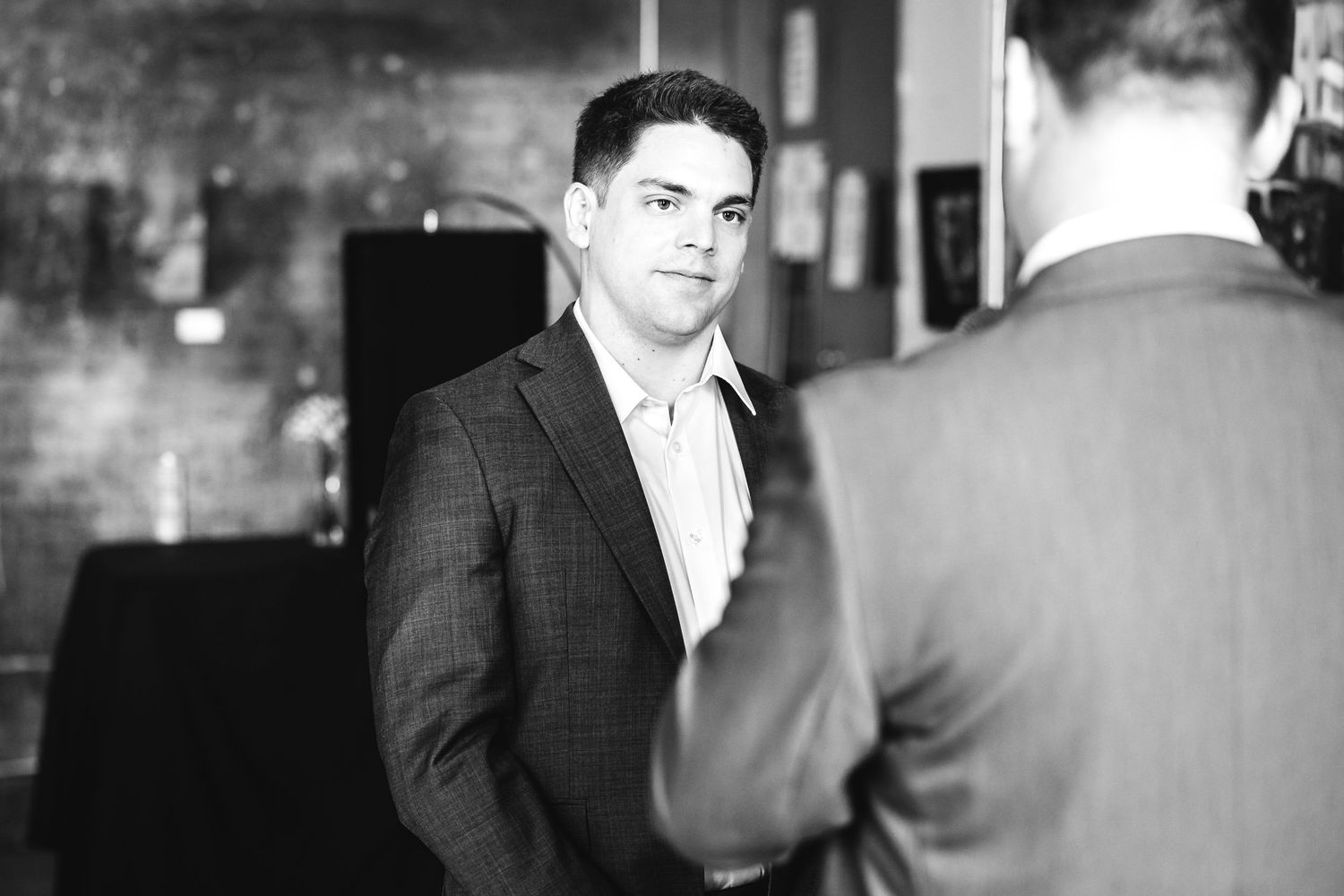 Black and white photo of two men in suits having a conversation at a formal event.