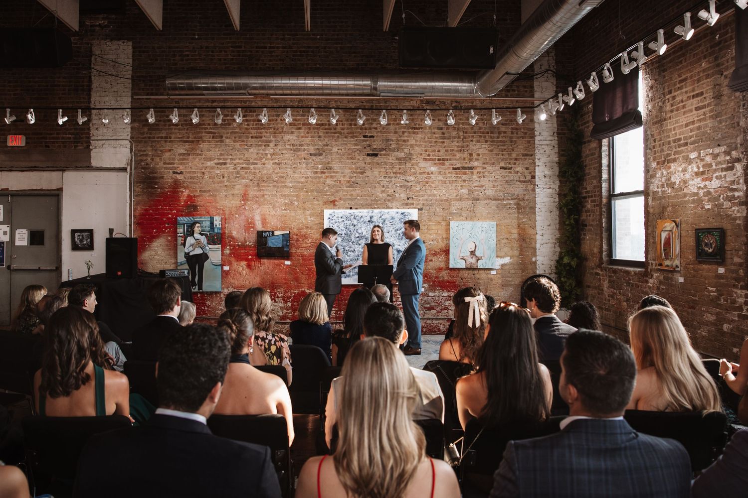 Guests seated at wedding ceremony in rustic brick venue with couple at altar.