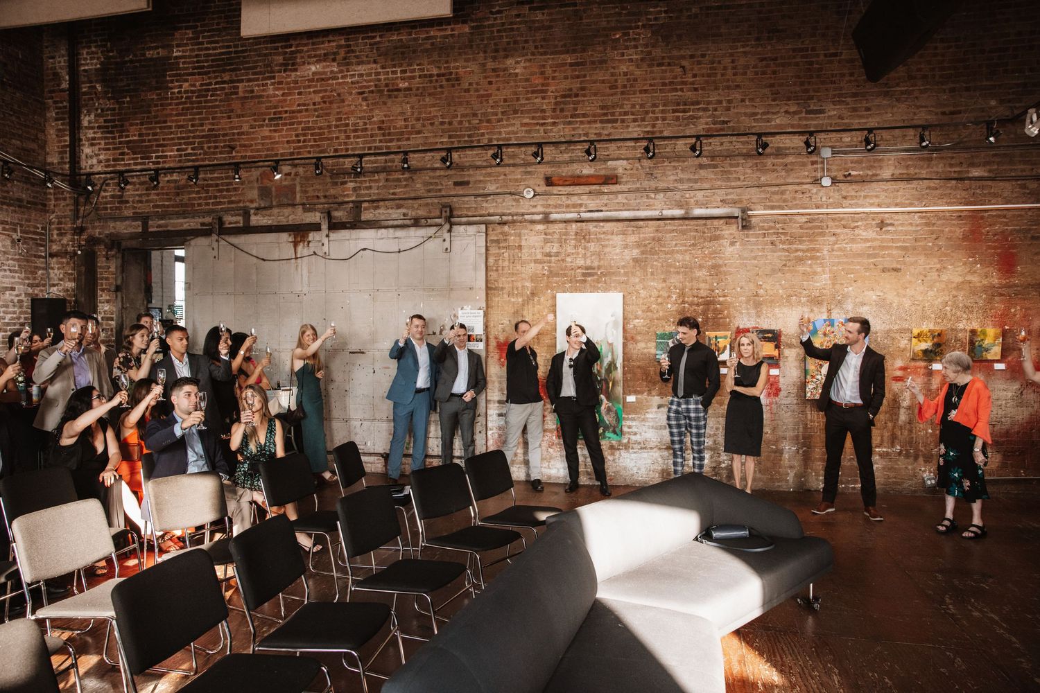 Crowd of guests standing and cheering in industrial brick venue with white furniture and chairs.