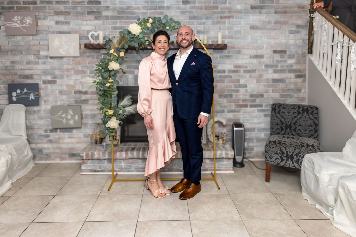 Couple in formal attire posing together in front of a stone fireplace with floral decor.