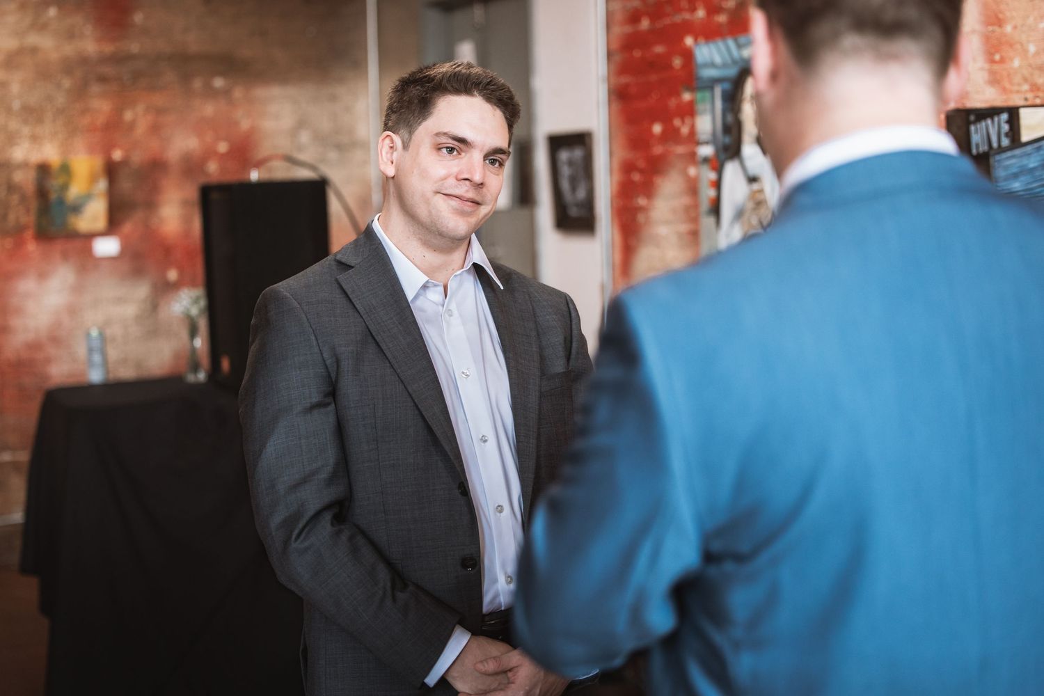 Man in gray suit smiles while shaking hands at a formal indoor networking event.