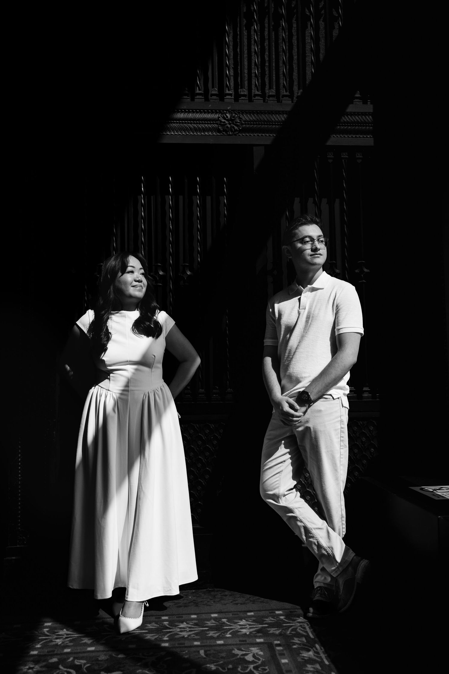 Couple poses in dramatic black and white near ornate dark woodwork.