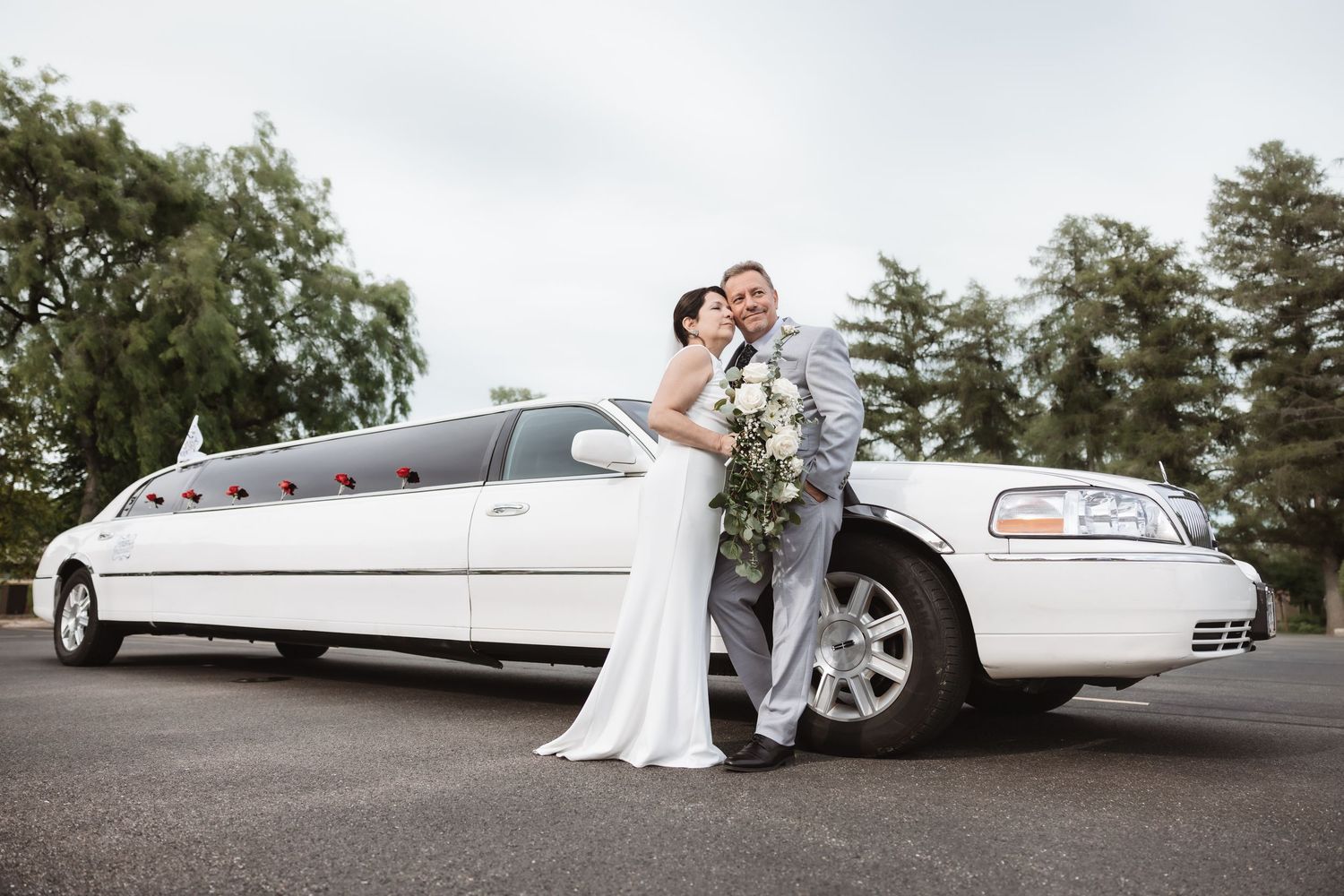 Bride and groom embrace in front of a white stretch limousine on their wedding day.