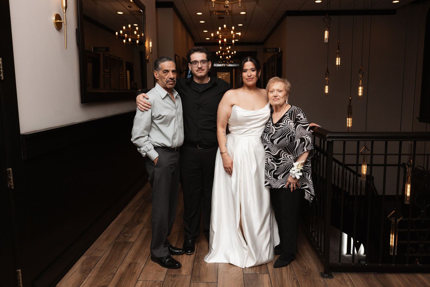 Bride in white gown posing with three family members in a warmly lit venue hallway.