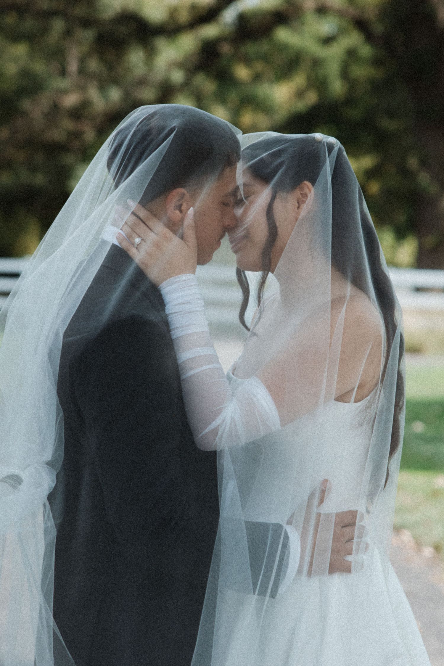 Bride and groom sharing an intimate moment under a flowing white veil outdoors on their wedding day.