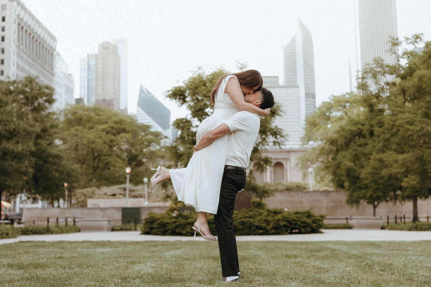 Couple sharing a romantic kiss lift in Chicago's Grant Park with city skyline in the background.