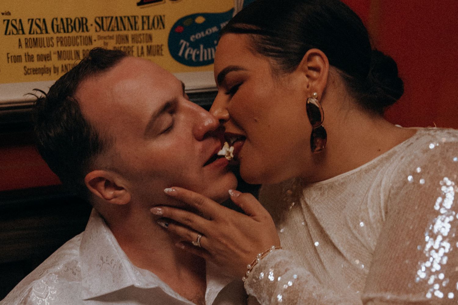 Bride and groom share a playful kiss in front of a vintage movie poster at reception.