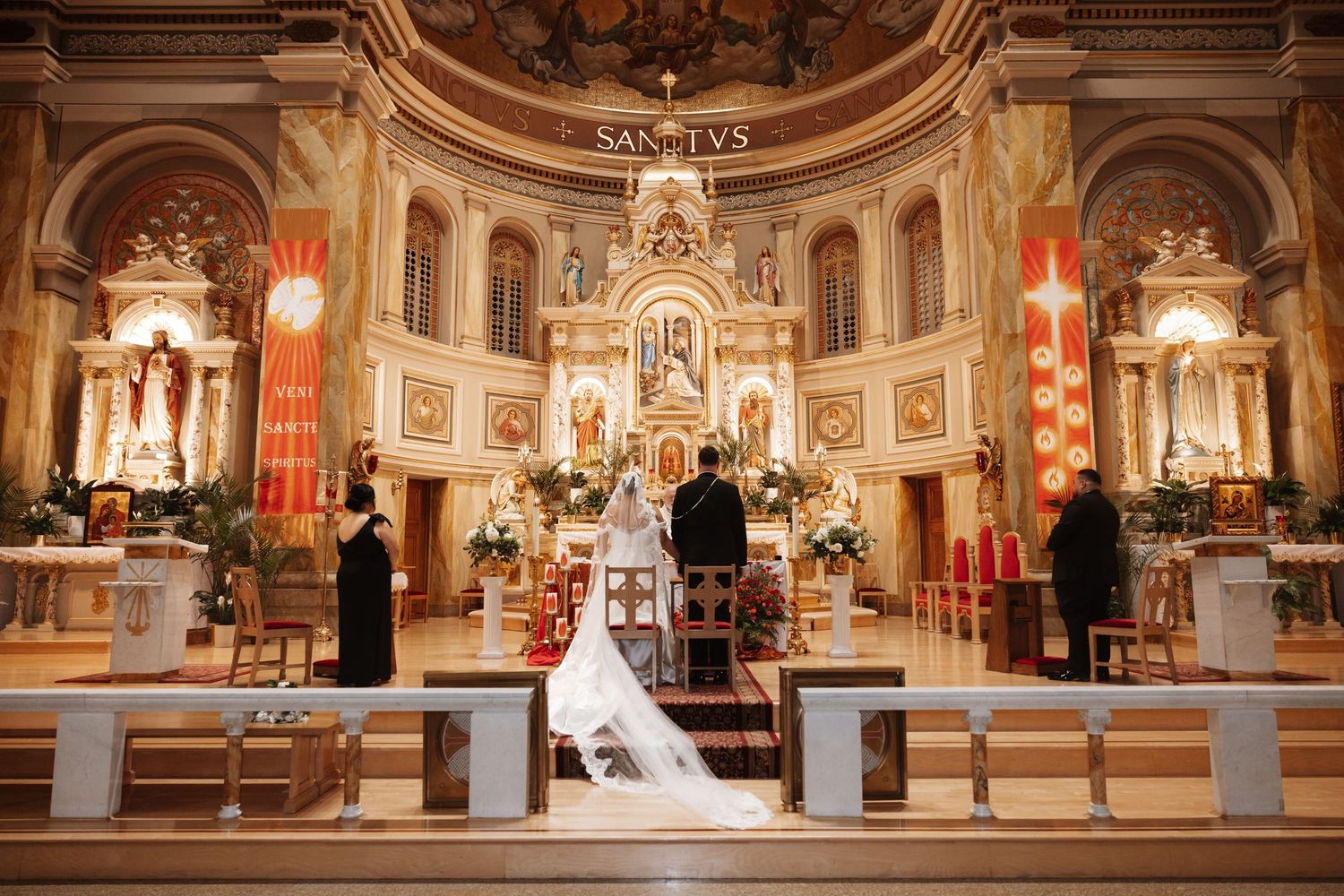 Bride and groom stand at the altar of a grand decorated church during their wedding ceremony.