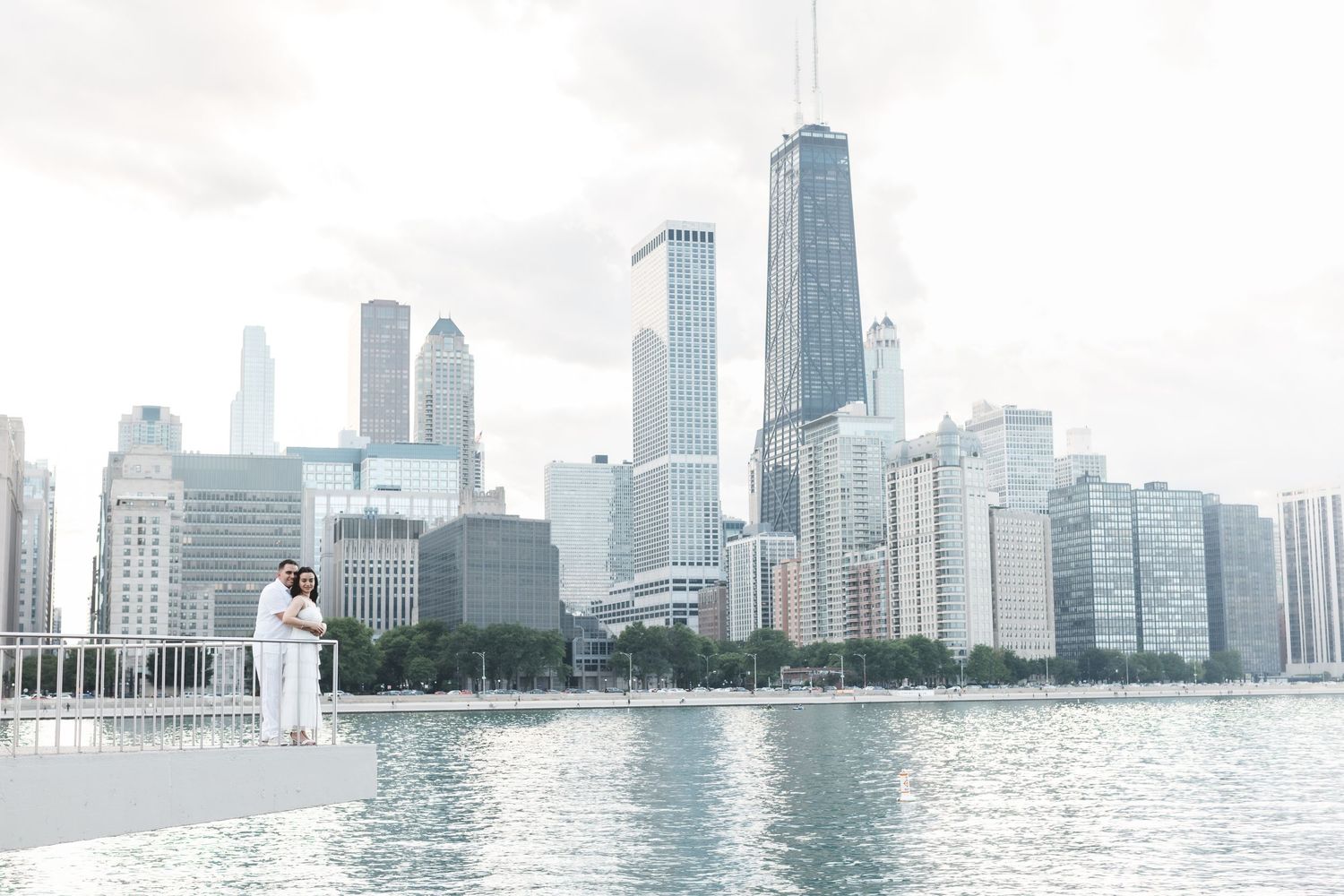 Couple in white attire poses on waterfront with Chicago skyline backdrop.