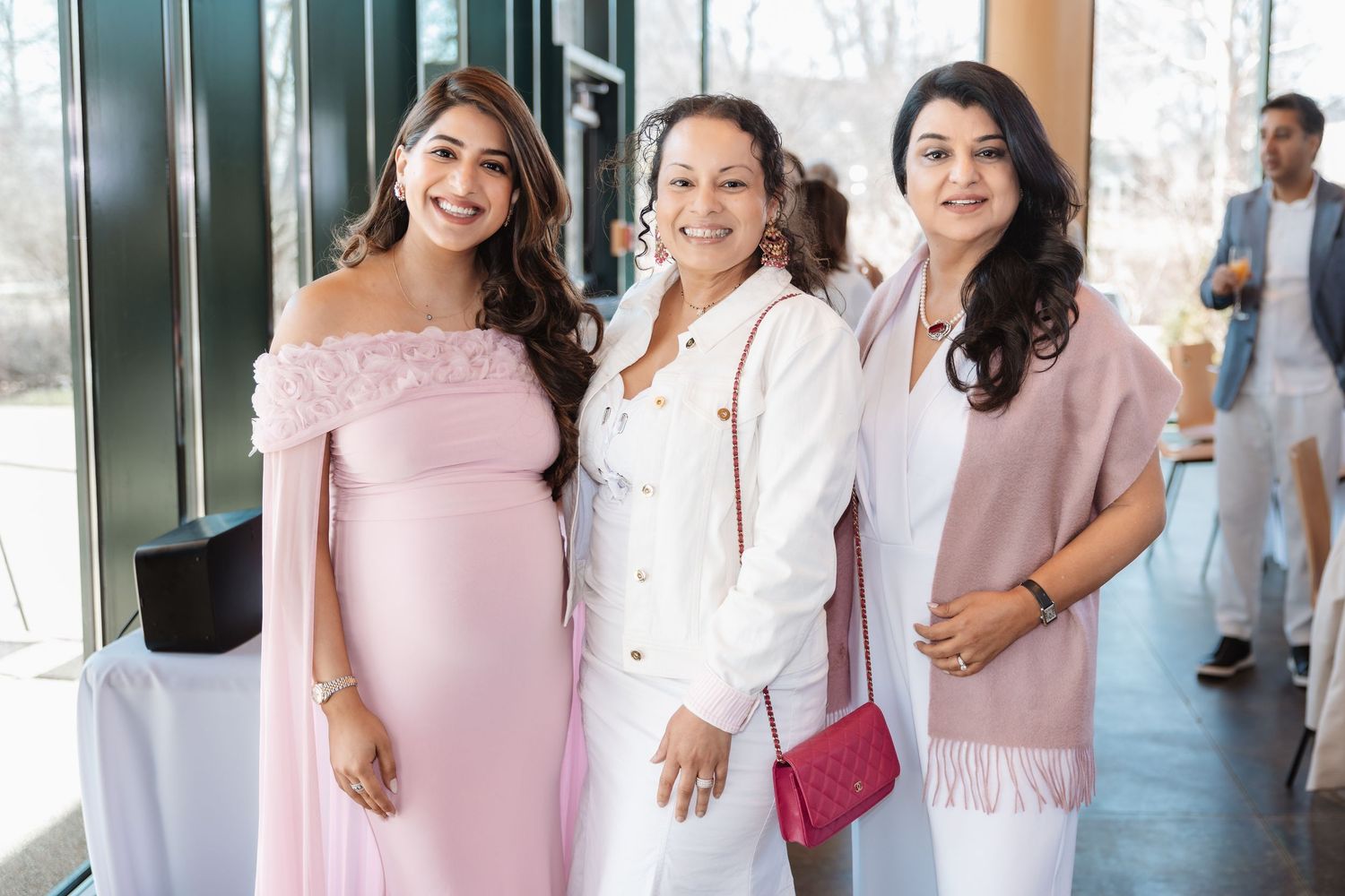 Three women pose together at baby shower, featuring pregnant guest in pink off-shoulder dress.