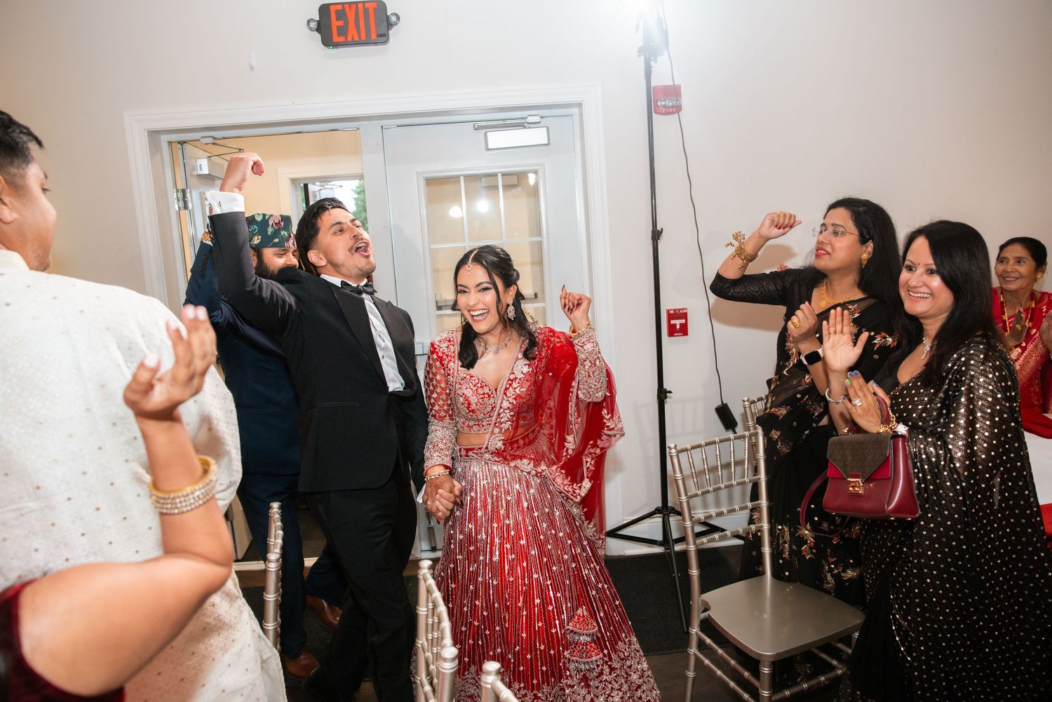 Guests celebrate bride in red bridal lehenga during Indian wedding reception entrance.