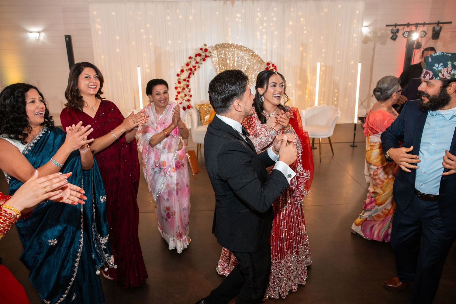 Bride in red lehenga shares first dance with groom surrounded by cheering guests.