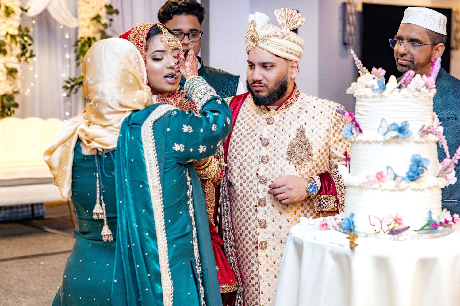 Wedding guests in traditional South Asian attire celebrating cake cutting ceremony.