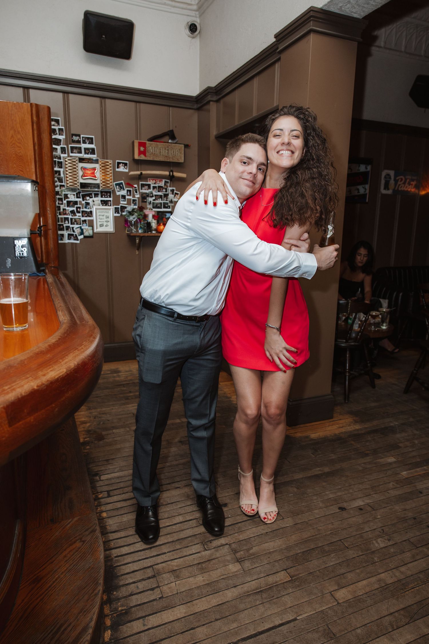 Smiling couple embracing at a wedding reception inside a warmly decorated bar venue.