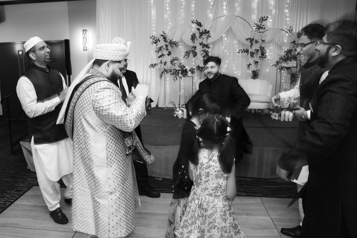 Black and white photo of men in traditional attire celebrating at a South Asian wedding.