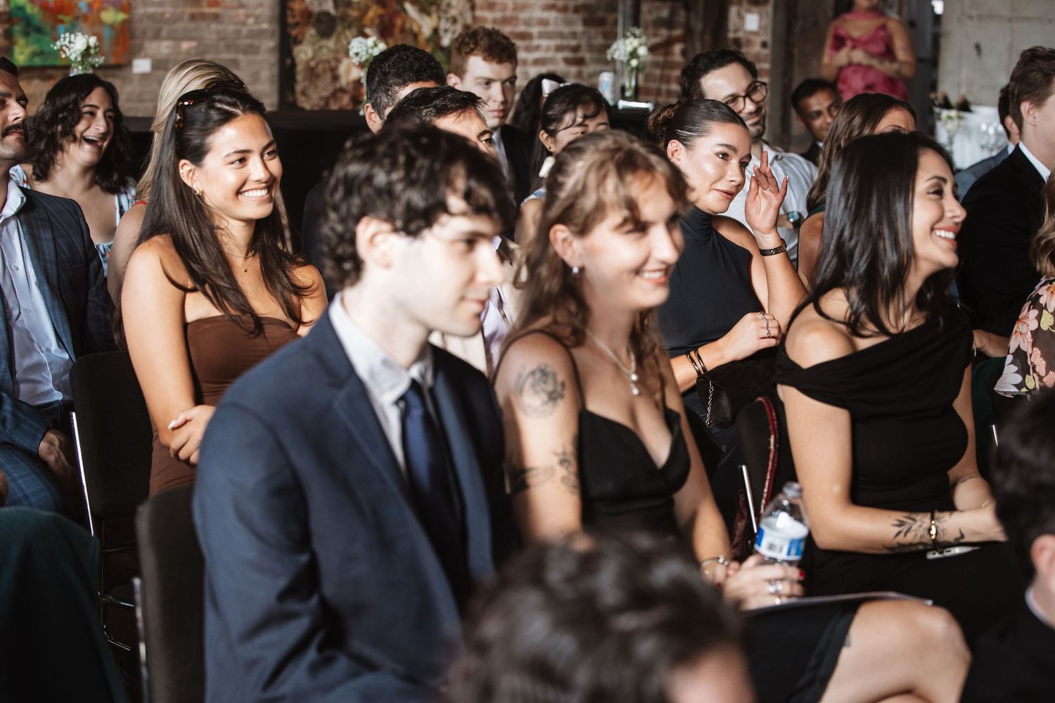 Diverse wedding guests laugh and smile while seated during a lively ceremony celebration.