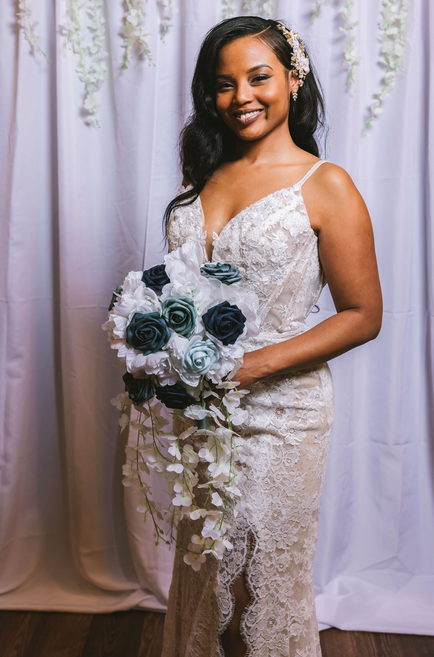 A smiling bride in a lace wedding dress holds a cascading bouquet of blue and white roses.