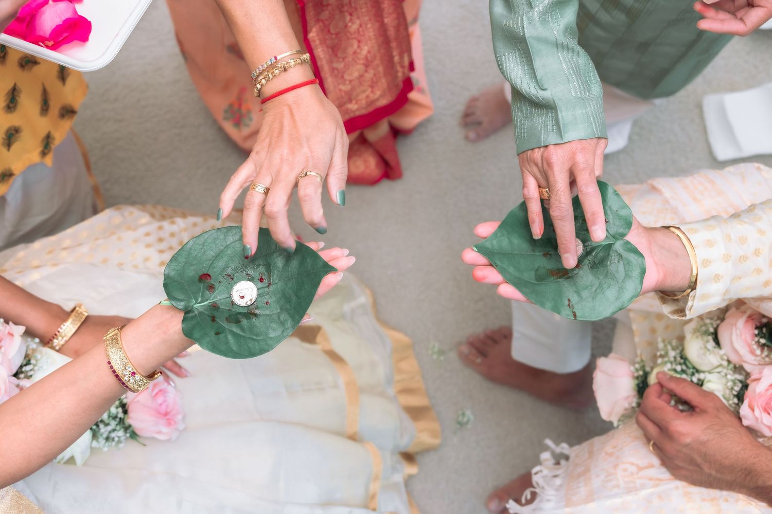 Top view of hands placing palms on green betel leaves during traditional Indian wedding ceremony ritual.