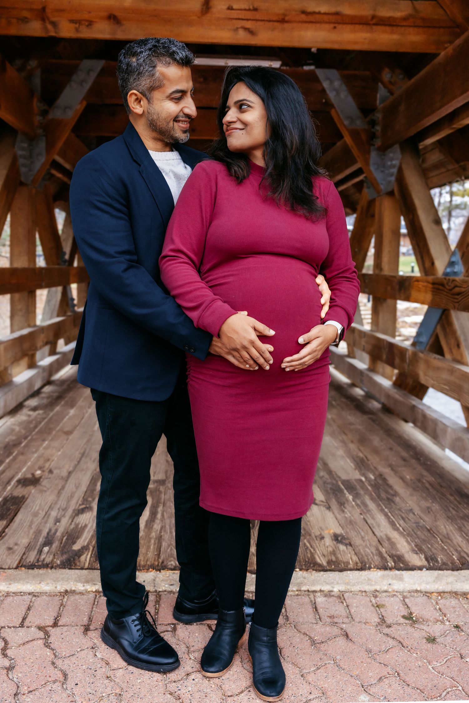 Couple sharing a tender moment on covered bridge during maternity photography session.