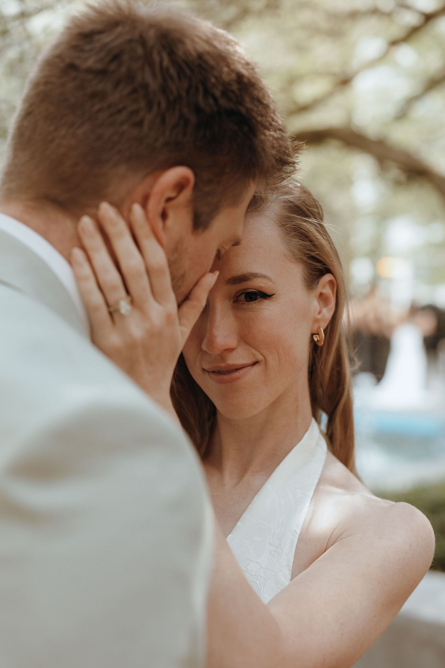 Bride tenderly cups grooms face during an intimate outdoor wedding moment.