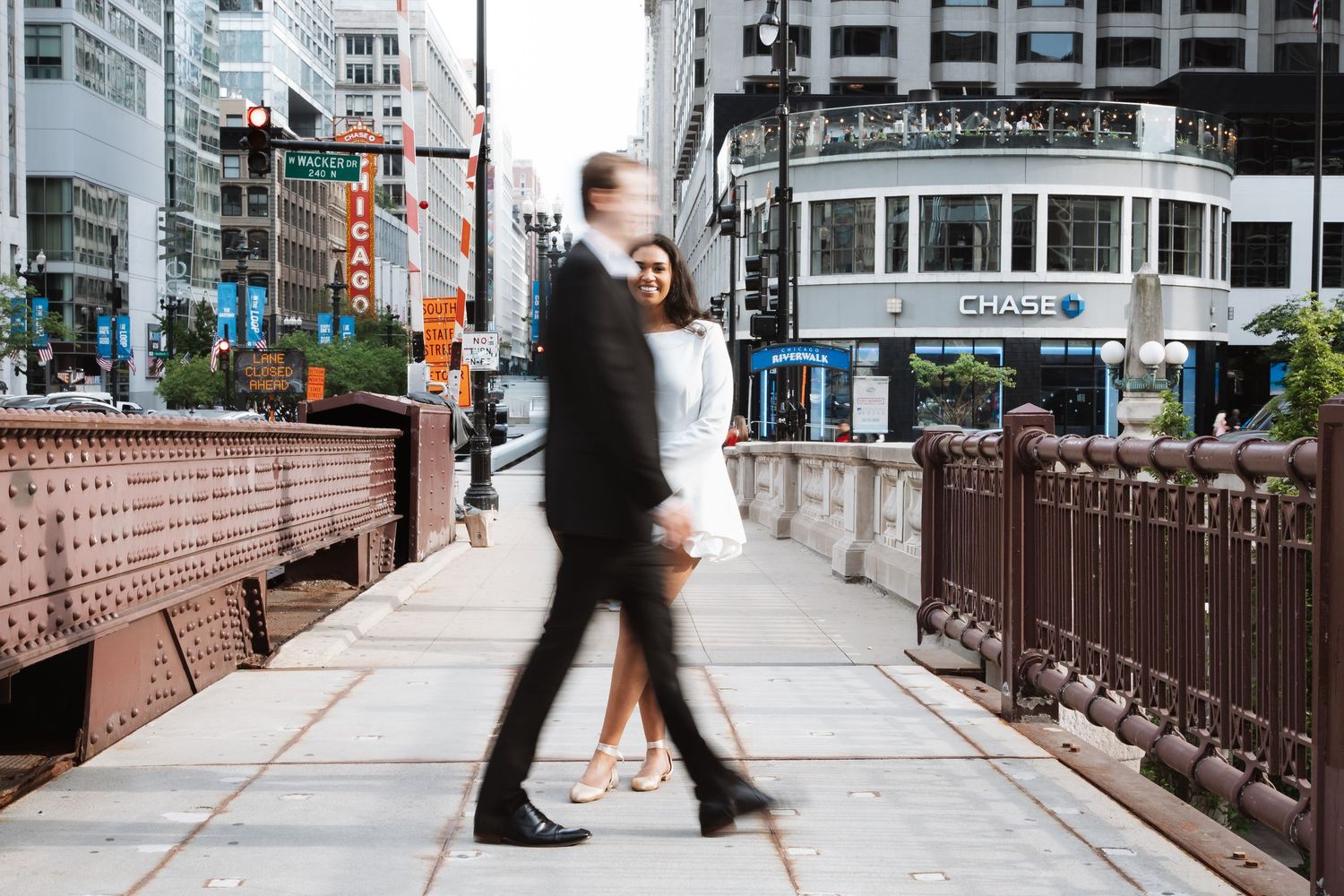 Couple walking hand in hand on a Chicago bridge with motion blur effect and city street scene behind them.