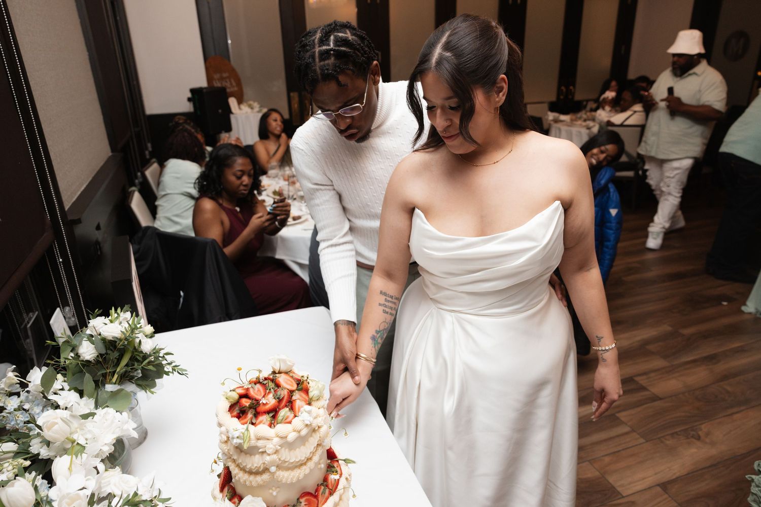 Bride in white strapless gown and groom cut decorated strawberry wedding cake at reception.