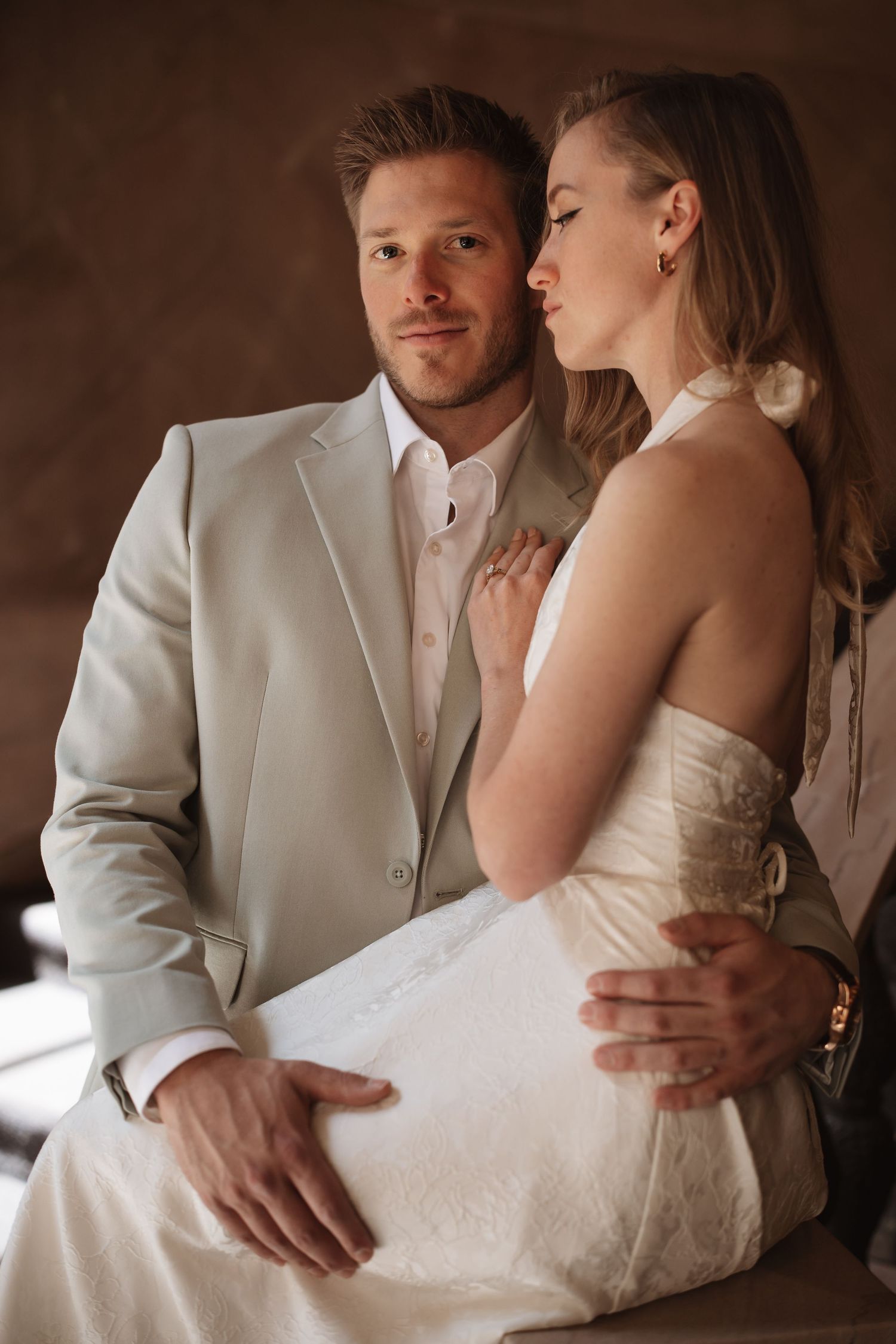 Bride and groom share an intimate moment, she in a white halter dress, he in a light gray suit.