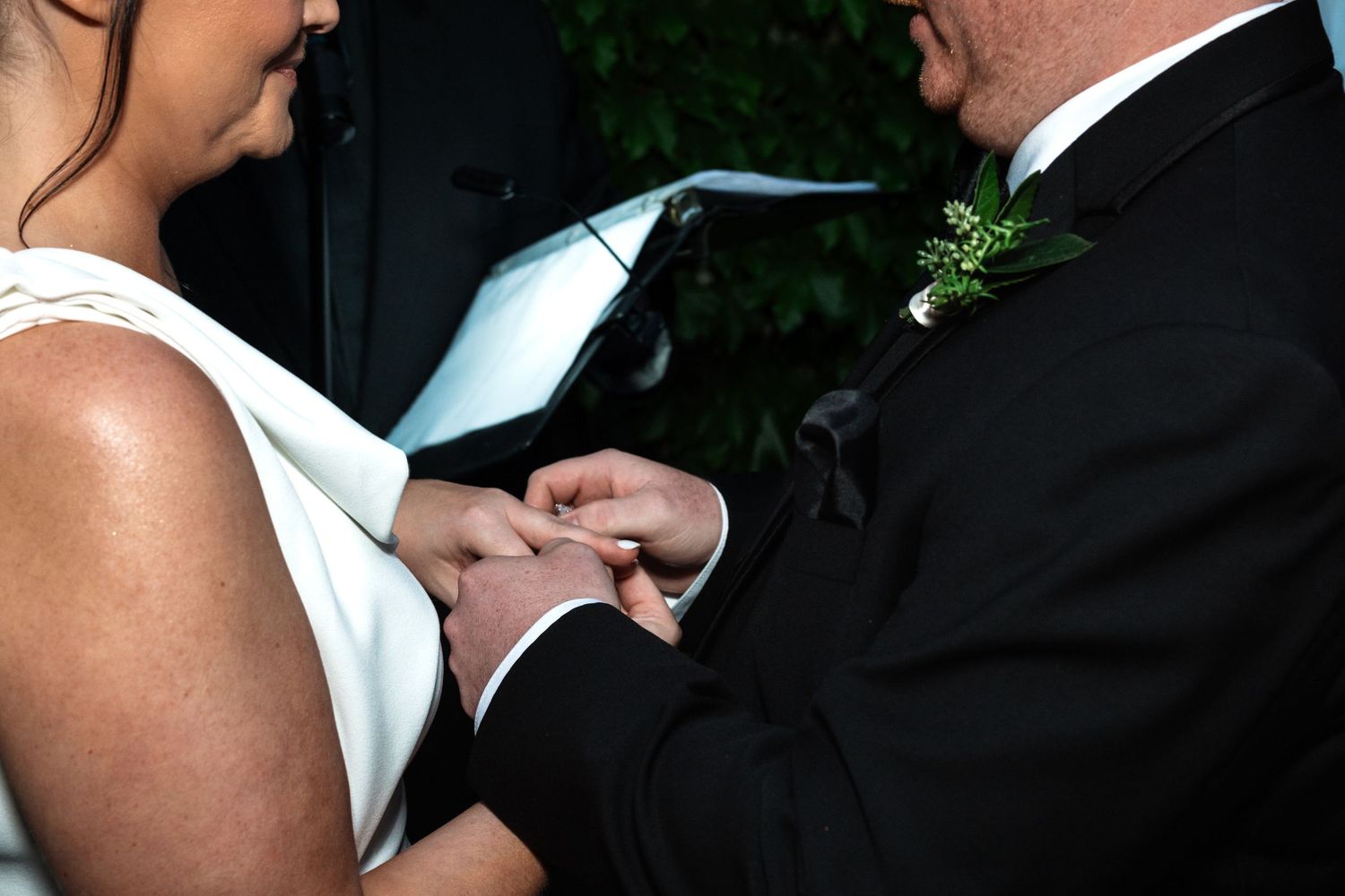 Groom places wedding ring on brides finger during intimate ring exchange at outdoor wedding ceremony.