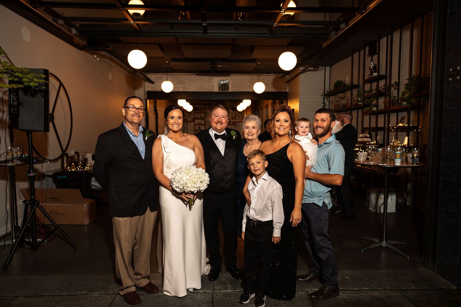 Family group photo with bride and groom posing at warmly lit wedding reception.