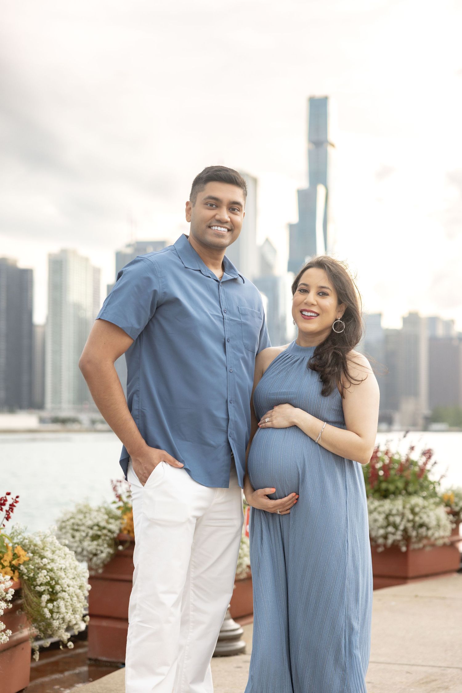 Smiling pregnant couple posing together near Chicago waterfront with colorful flowers and city skyline.