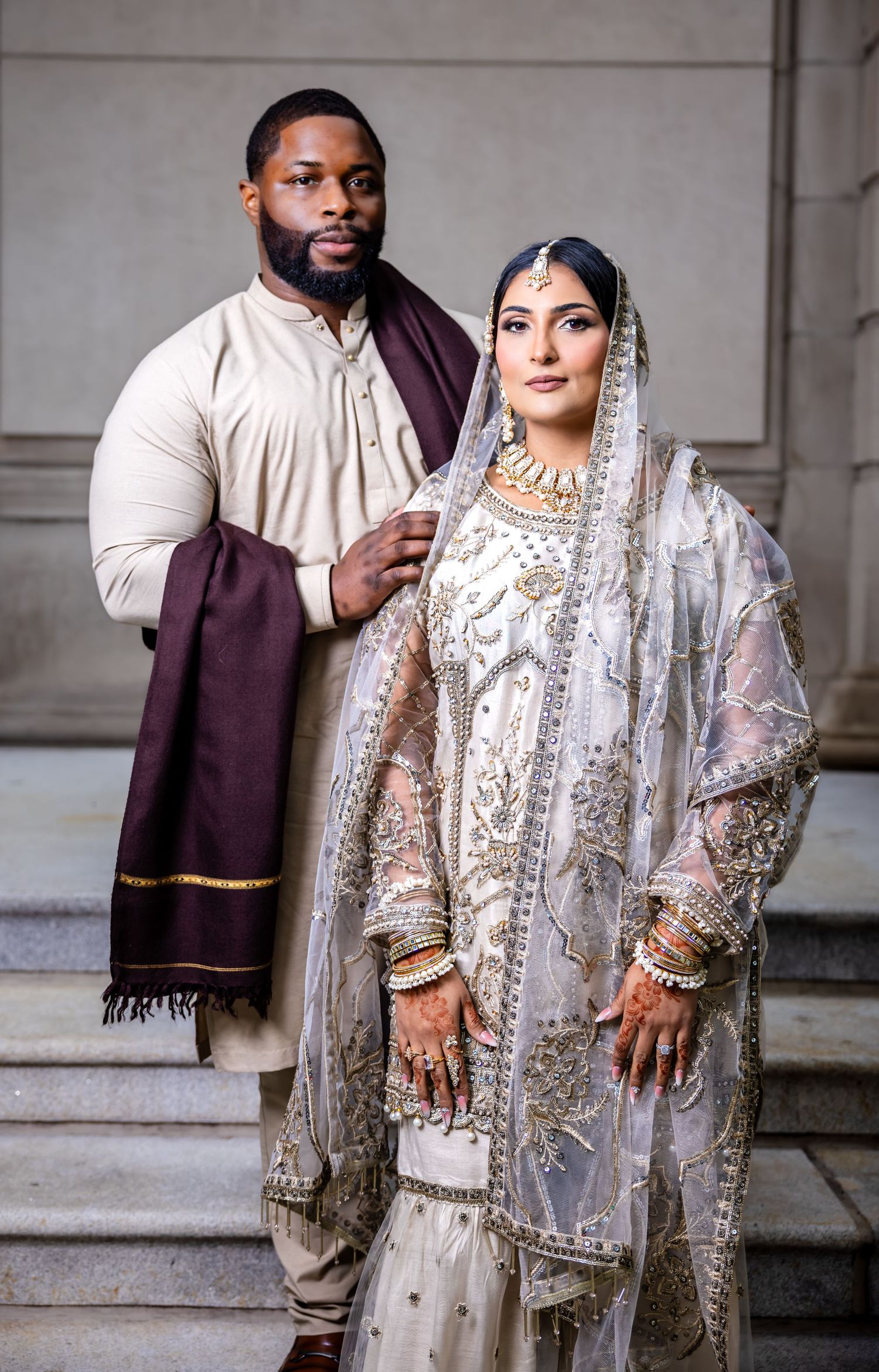 South Asian bride in white embroidered lehenga with groom in cream kurta posing together at Islamic wedding ceremony.