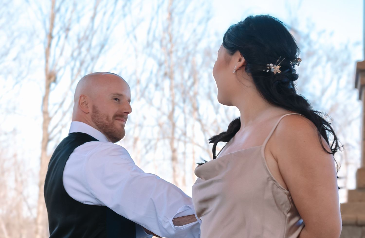 Groom in navy vest smiles at bride in blush gown during romantic outdoor wedding dance.
