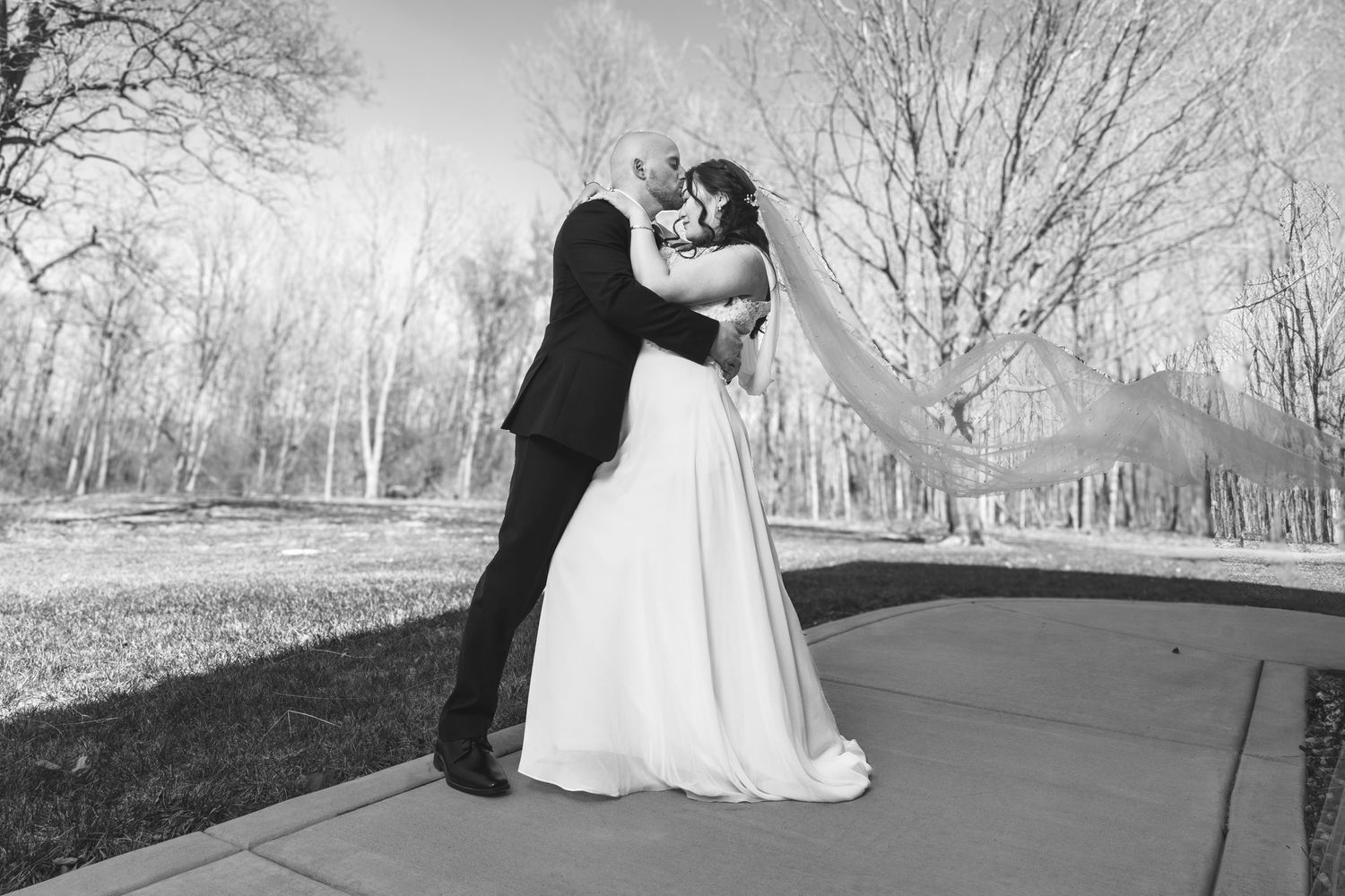 Black and white photo of bride and groom sharing romantic kiss outdoors on wedding day.