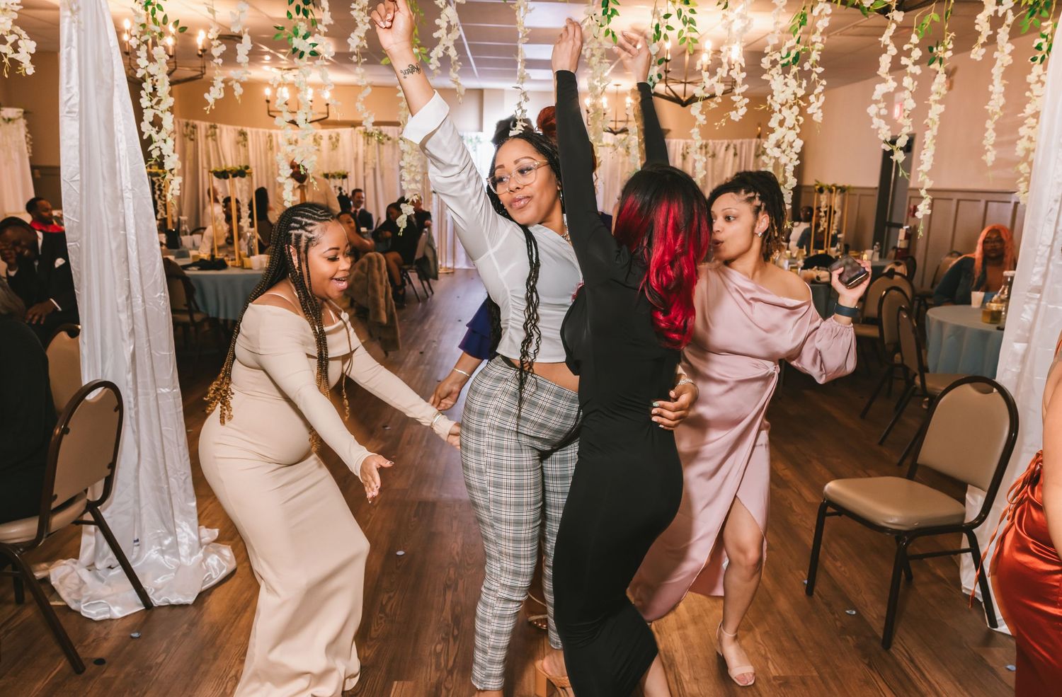 Three women dance energetically together on the dance floor at a vibrant wedding reception.