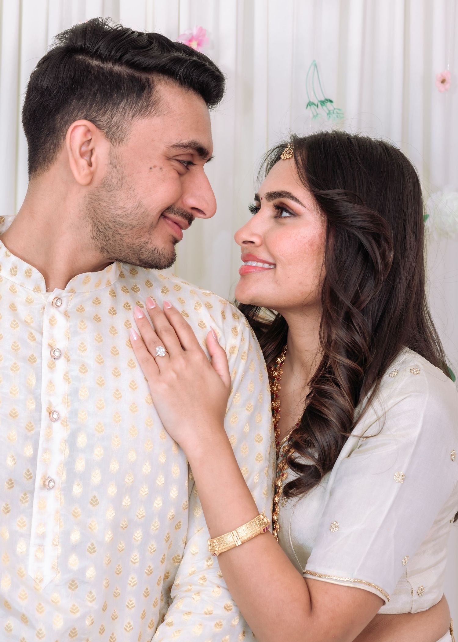 South Asian couple in white traditional wedding attire gazing at each other lovingly during ceremony.