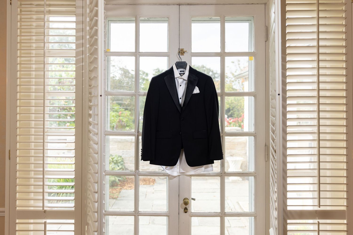 Groom's black suit with tie hanging on French doors in natural light.