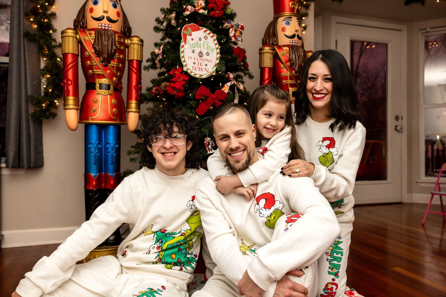 Smiling family of four in matching Grinch Christmas sweatshirts posing in front of a festive holiday tree.