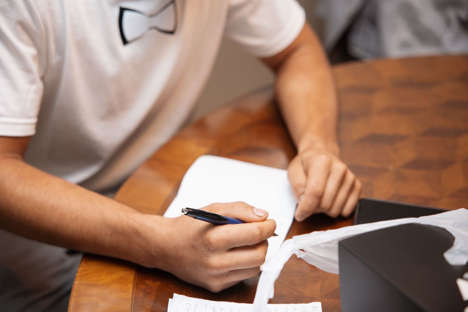 Groom signing wedding documents at wooden table wearing white t-shirt with bow tie graphic design.