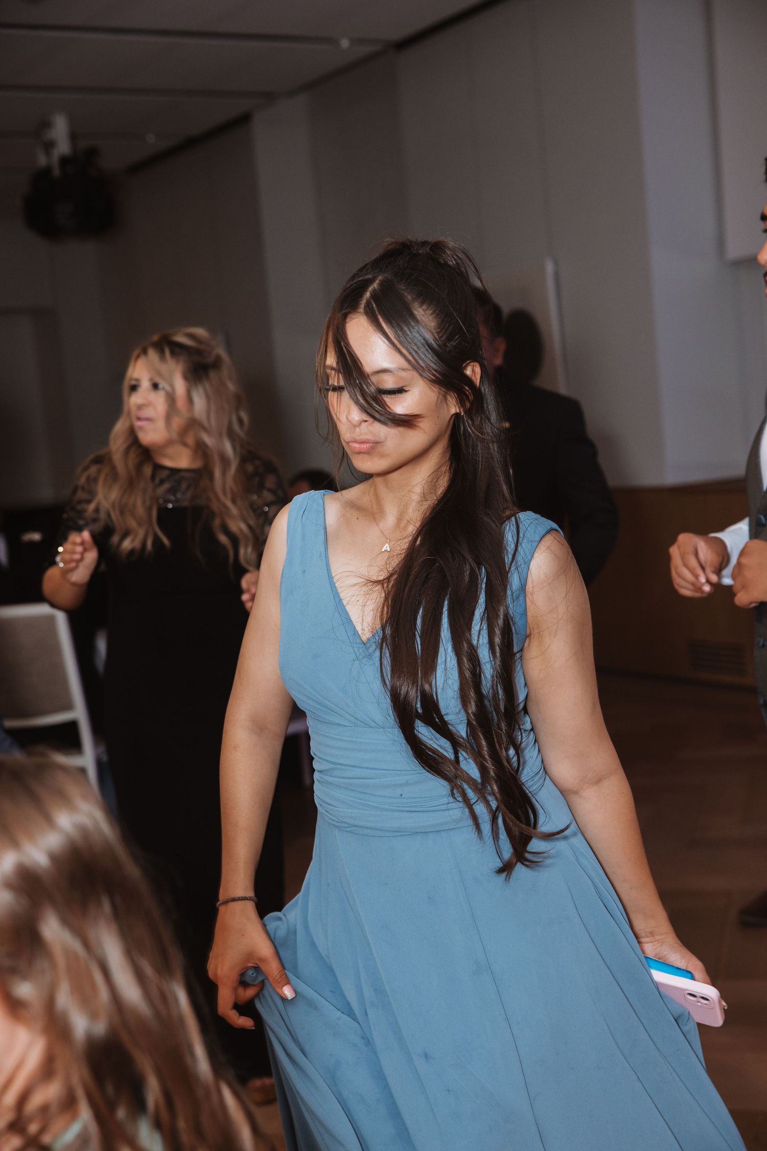 Woman in blue bridesmaid dress dancing at wedding reception with long dark flowing hair.