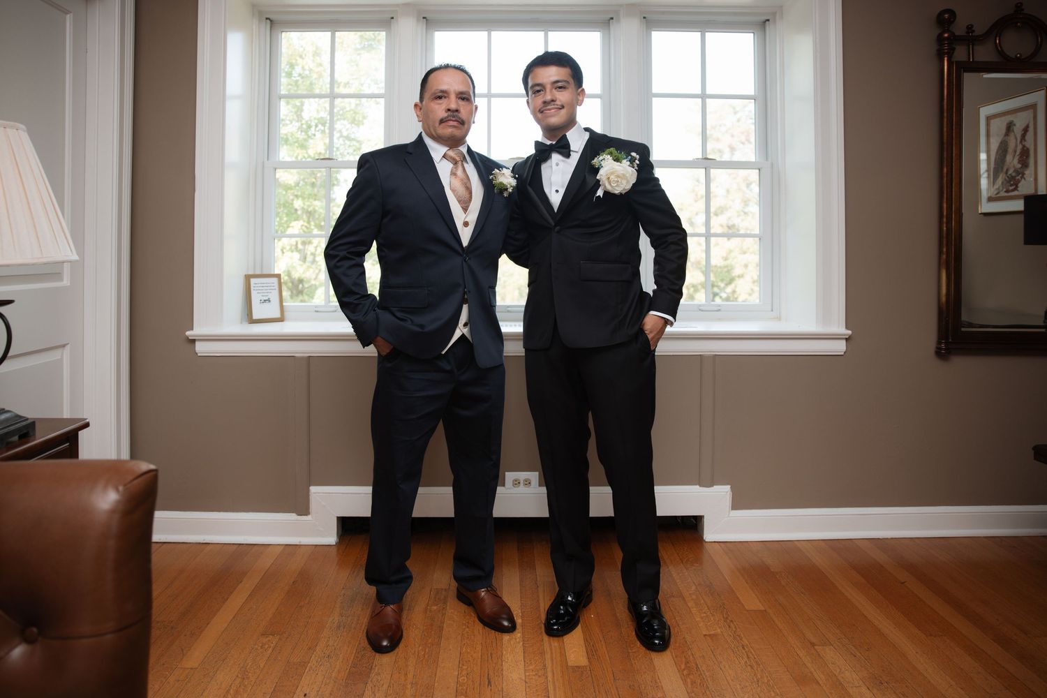 Groom and father posing in suits before wedding ceremony indoors.