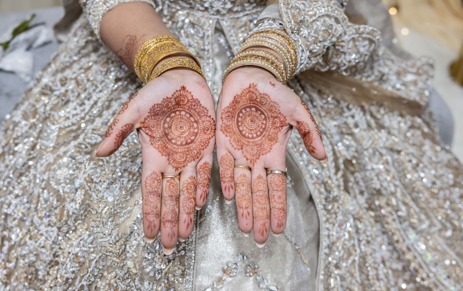 Bride displays intricate henna mehndi designs on both palms adorned with gold bangles in traditional South Asian wedding.
