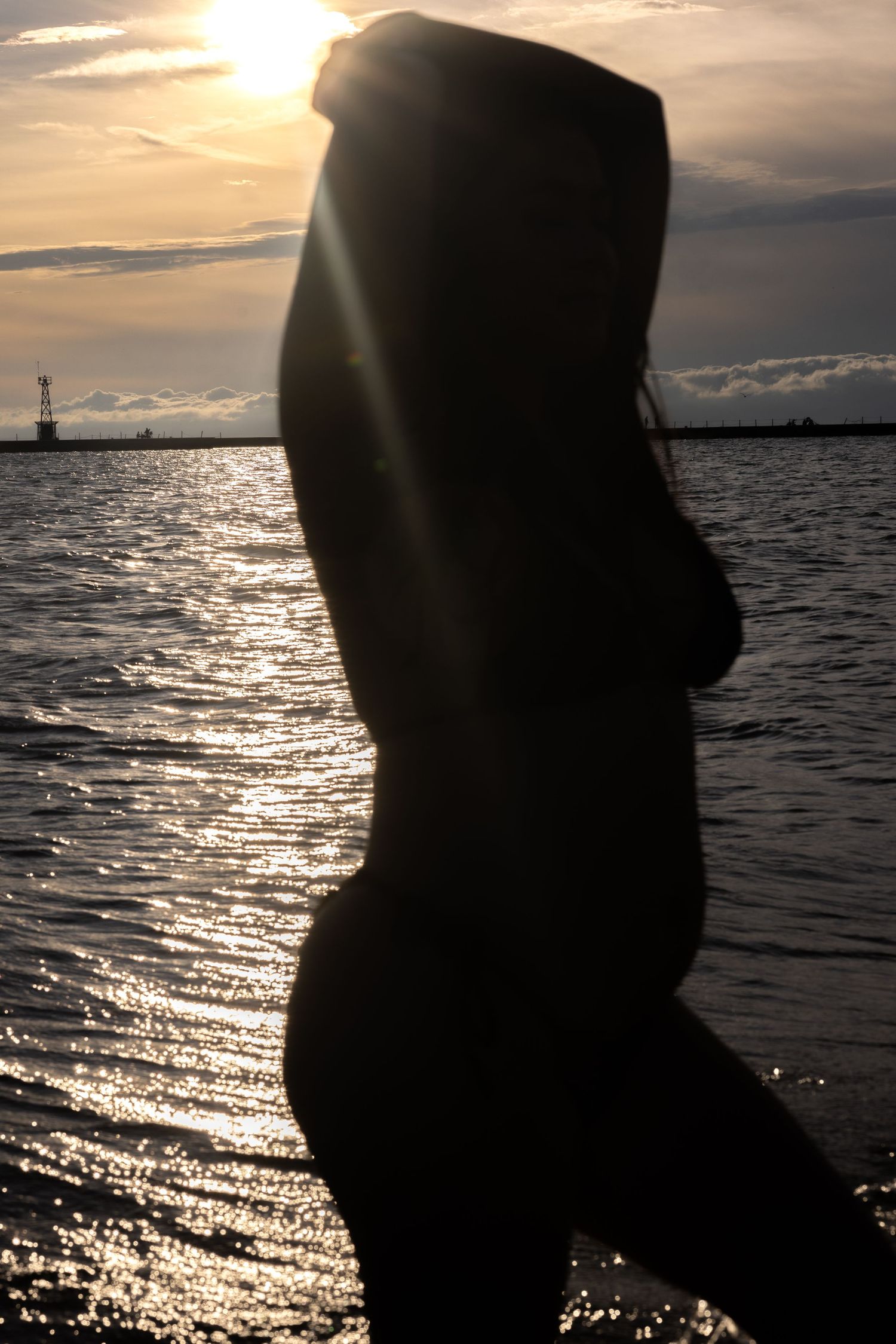 Silhouette of woman standing in water with sun setting over ocean horizon.