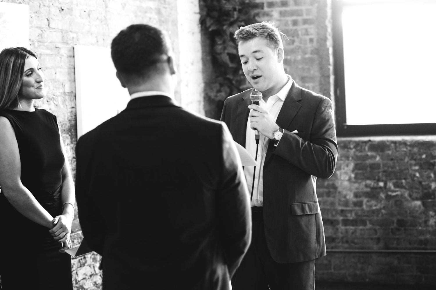 Black and white photo of man speaking into microphone at a formal ceremony.